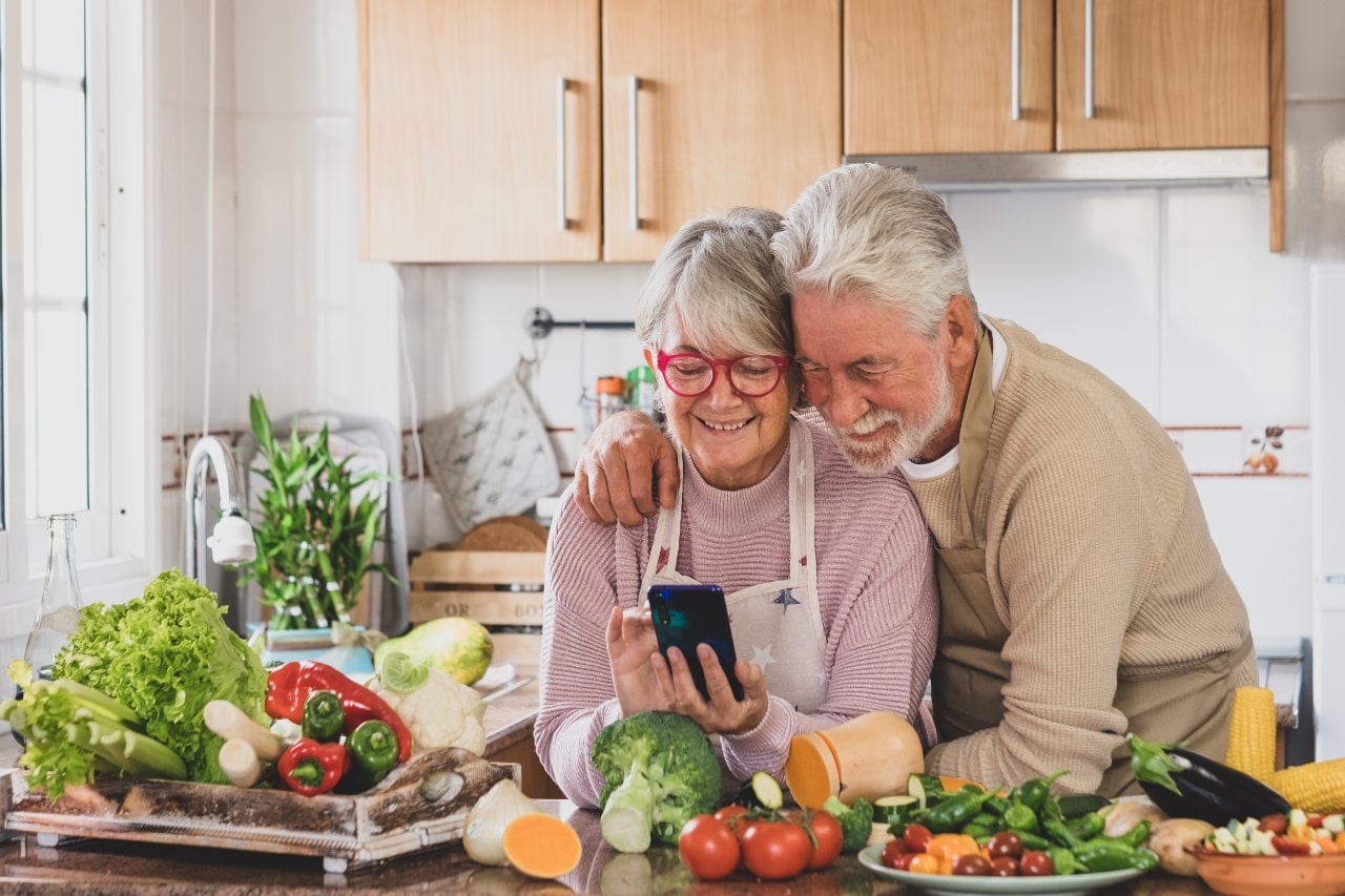 pareja de adultos mayores con hábitos saludables miran juntos una receta en el celular frente a vegetales