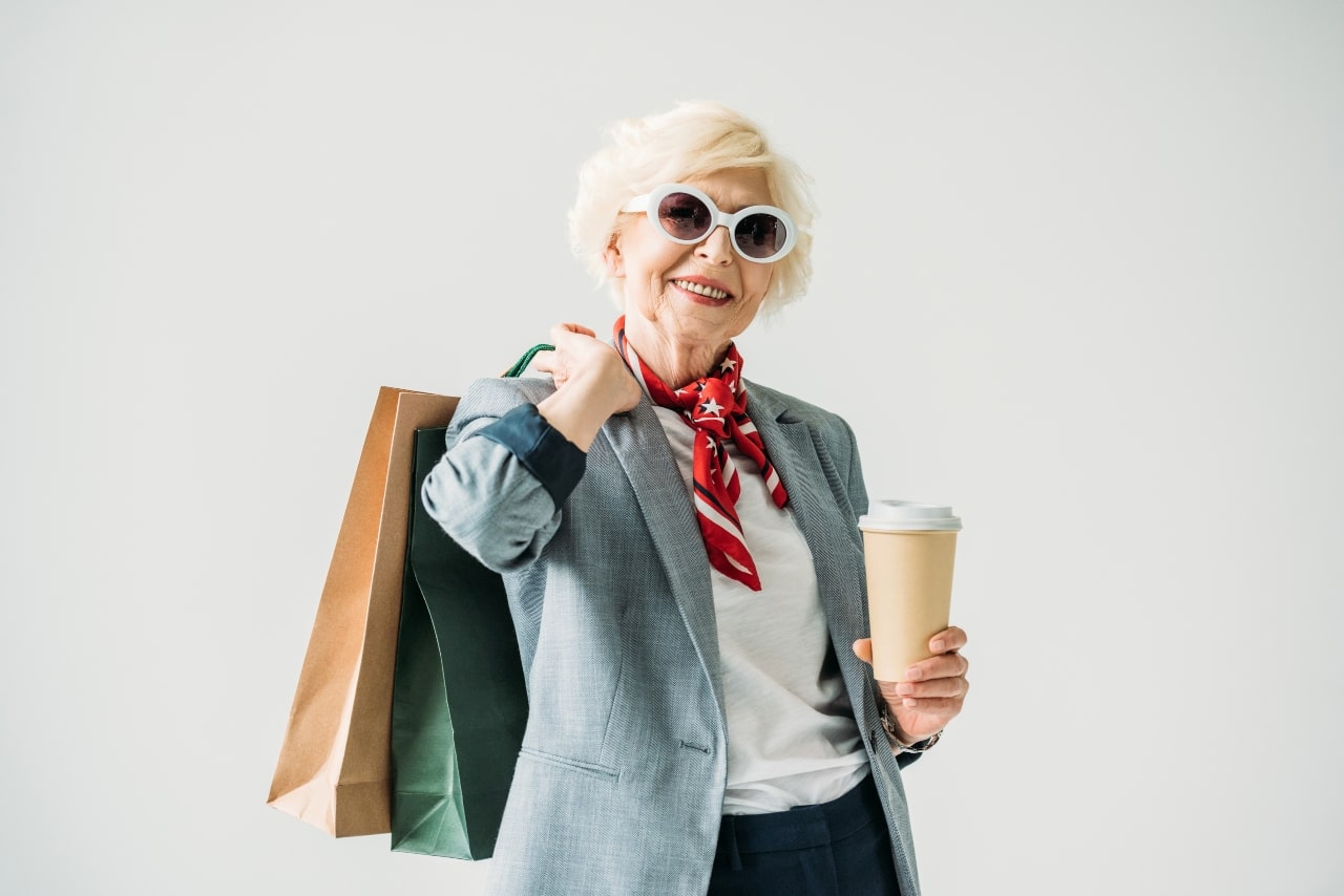 Mujer mayor de edad a la moda, con bolsas de compras y café.