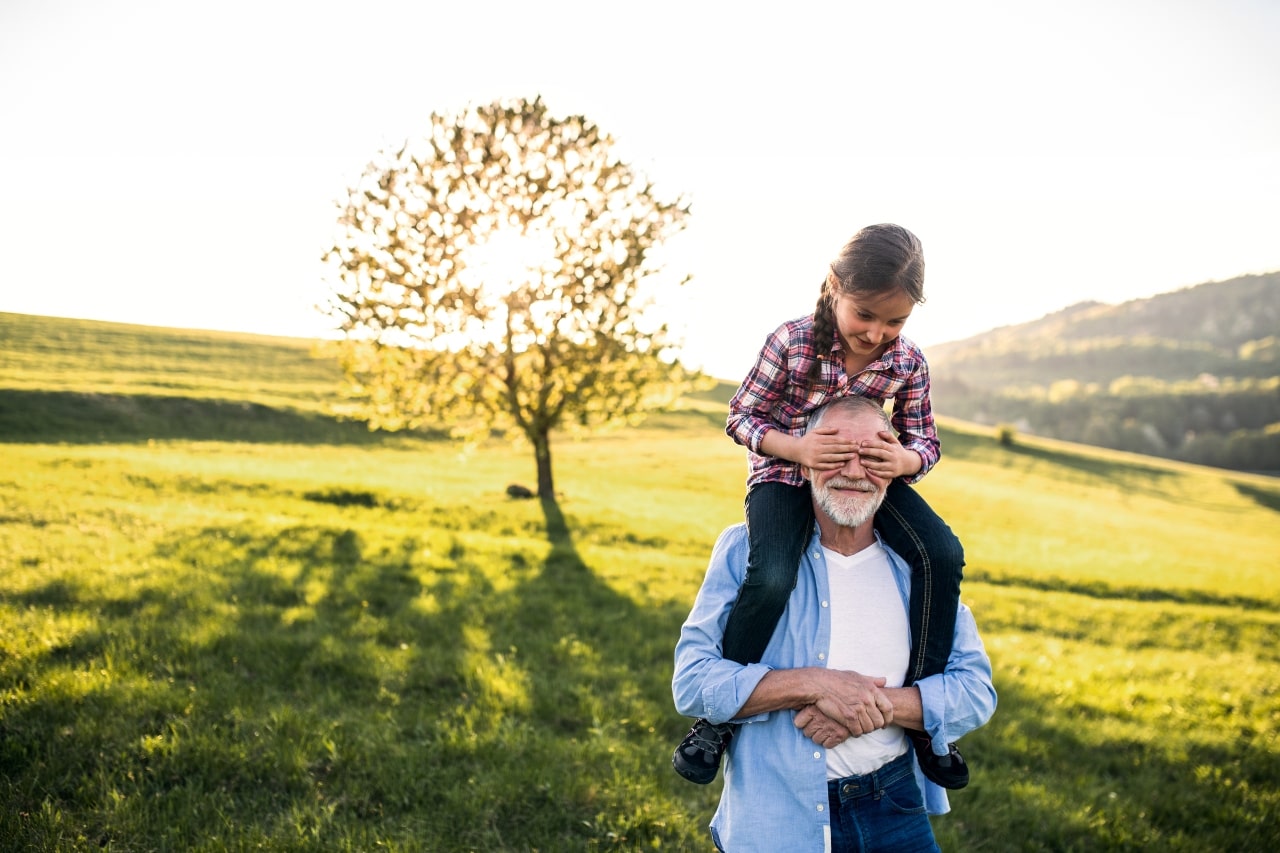 Abuelo dando a su nieta un paseo en la naturaleza mientras ella tapa sus ojos en un atardecer 