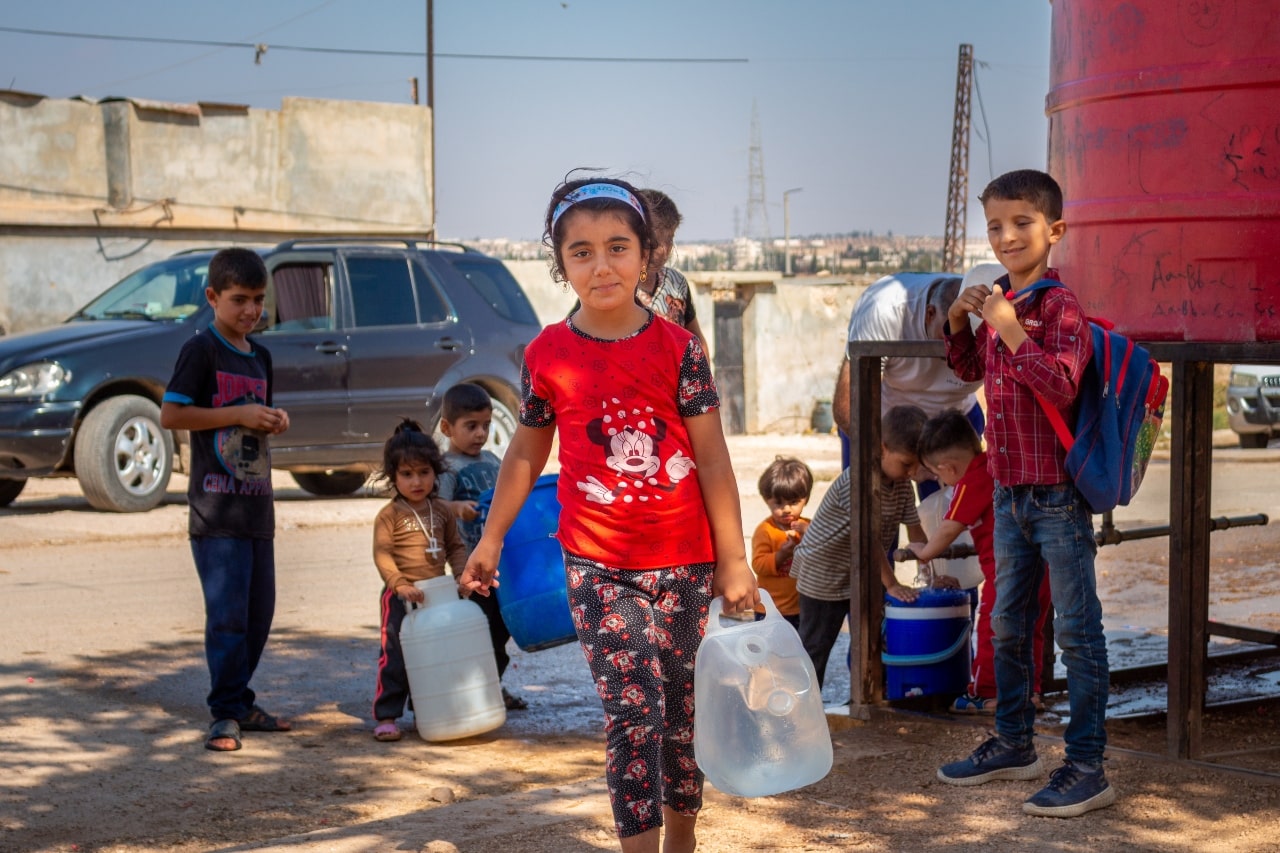 Niños y niñas recogiendo agua de un tanque para llevar a sus casas.