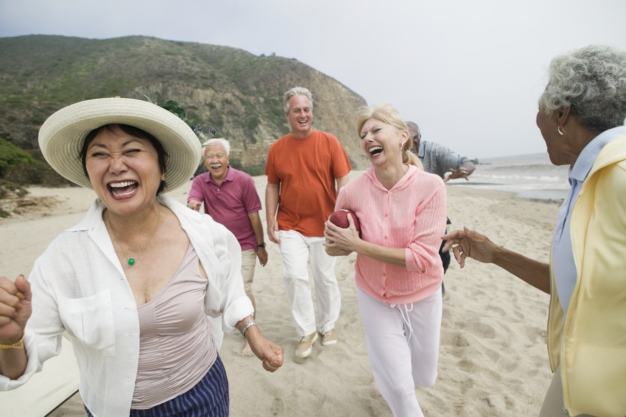 Amigos mayores de edad corriendo en la playa mientras ríen y disfrutan la vida 