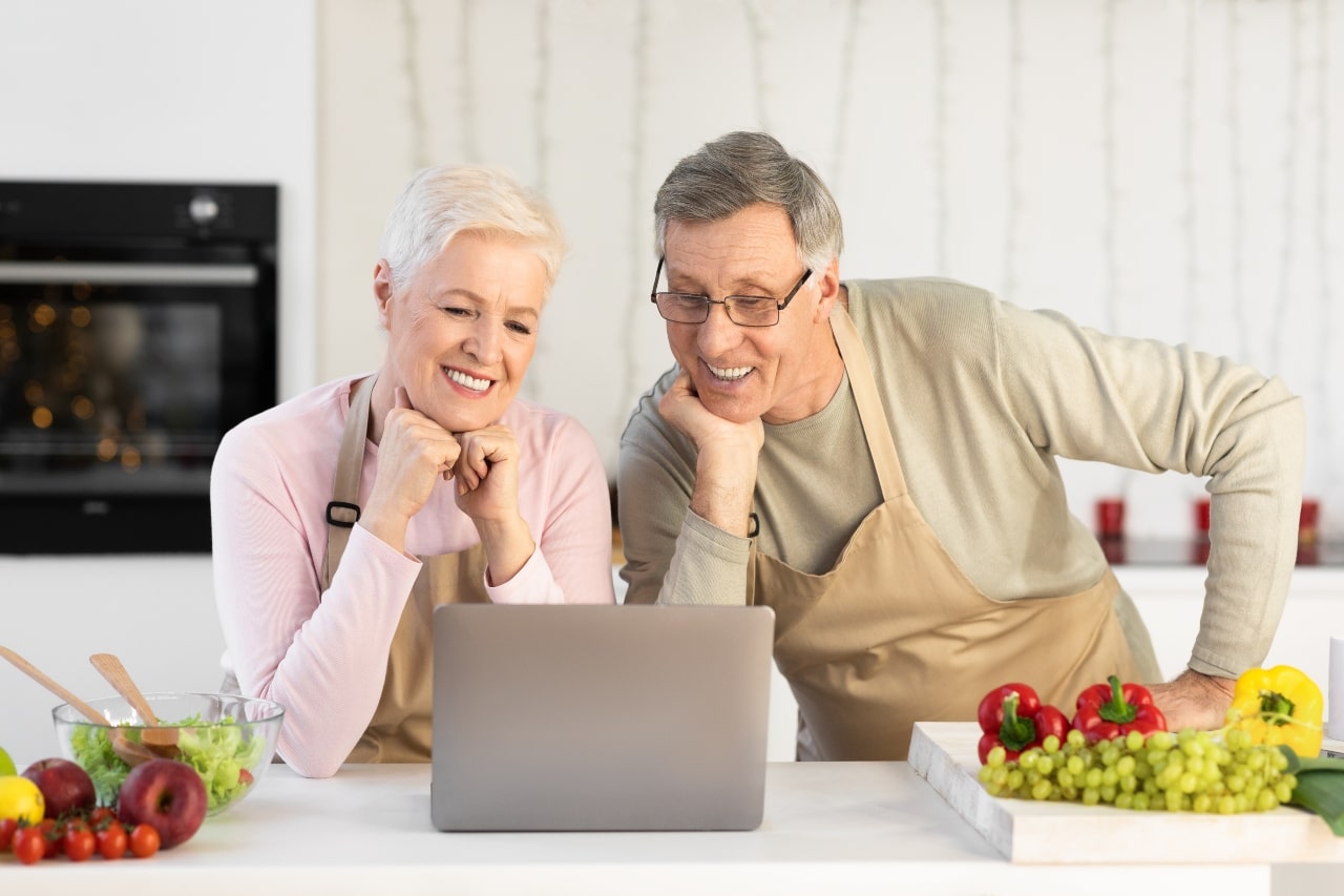 Pareja feliz haciendo cursos online para adultos mayores sobre cocina