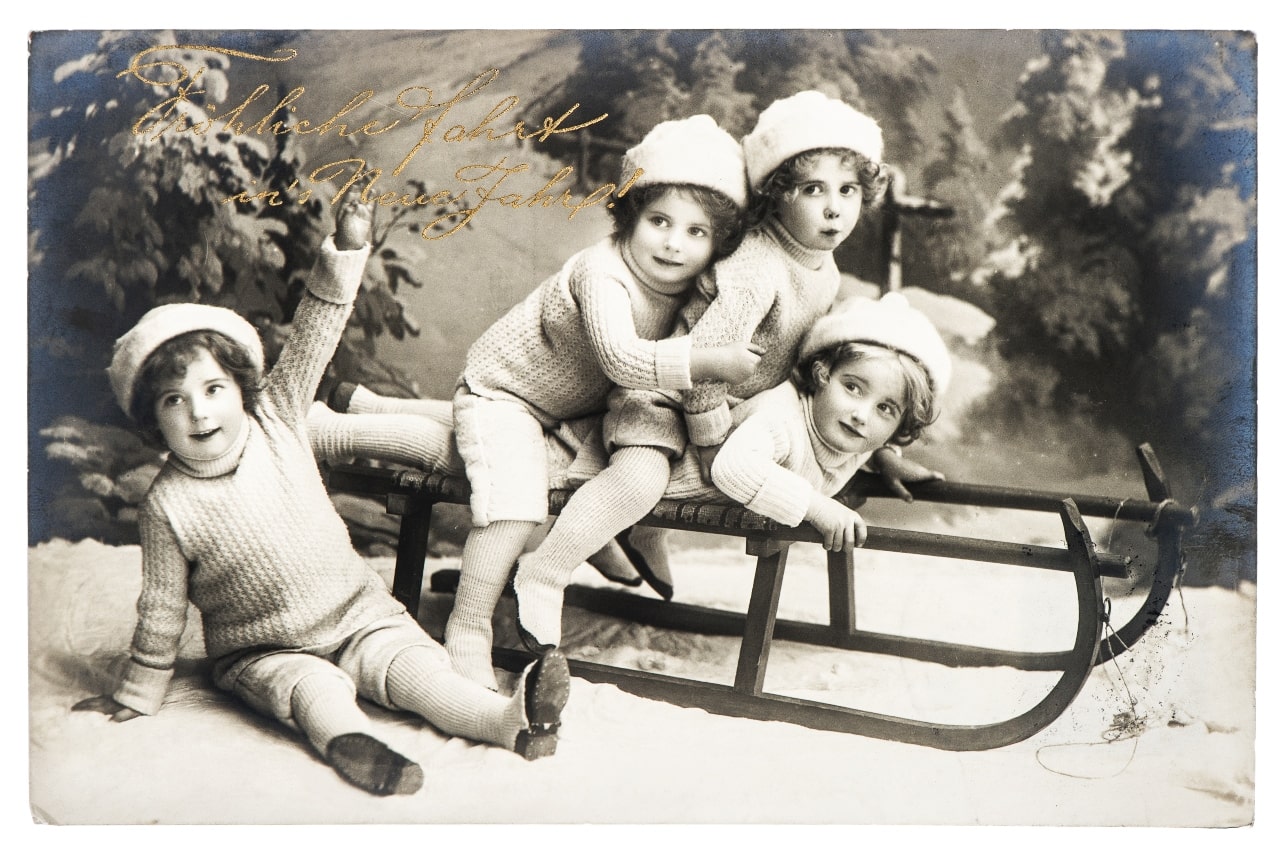 un grupo de hermanos pequeños disfrutan de la navidad en Alemania, en 1910, montados encima de un trineo y rodeados de árboles navideños.