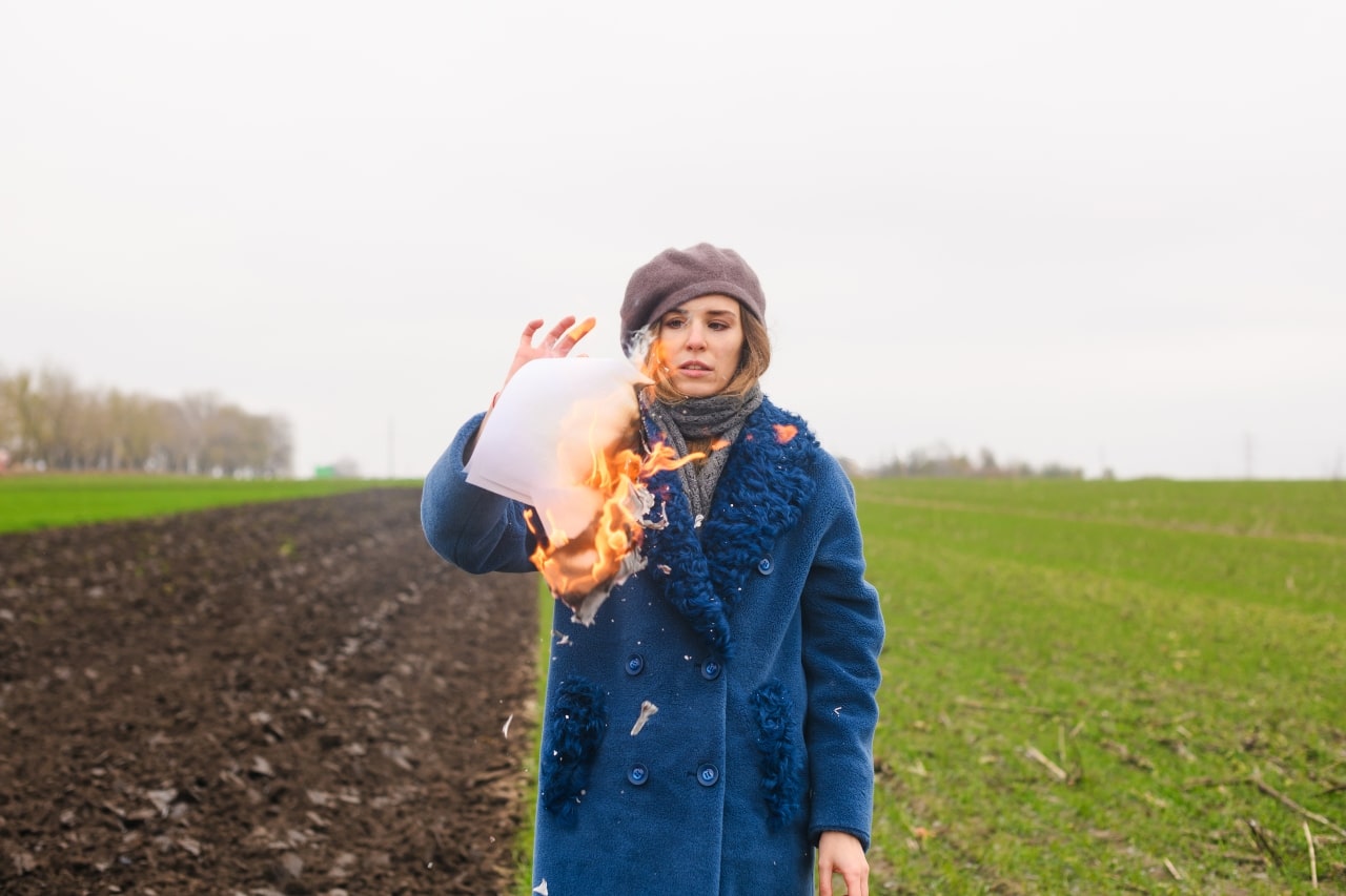 mujer de corta edad de pelo rubio quema un papel en la mitad de un campo frío y solitario, como símbolo de una nueva vida.