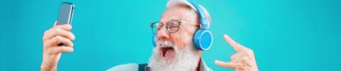Hombre mayor con audífonos y tatuajes se toma una foto divertida frente a su celular 