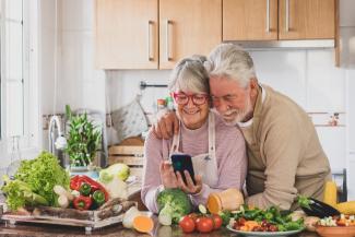pareja de adultos mayores con hábitos saludables miran juntos una receta en el celular frente a vegetales