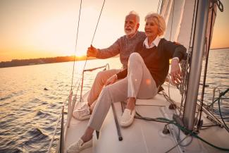 hombre de 60 años disfrutando de la compañía de una mujer mayor en un yate mientras contemplan el atardecer.
