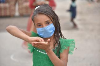 Niña de siete años de edad con tapabocas y vestida de verde haciendo un movimiento con sus manos