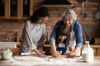 Abuela, mamá e hija se divierten amasando con un rodillo una preparación en la cocina