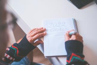 Manos de anciana escribiendo las metas del año 2022 en un diario.