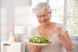 señora adulta comiendo una ensalada verde y sonriendo.