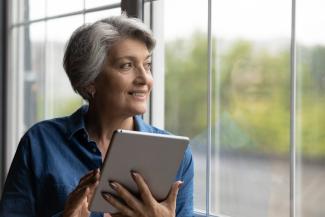 Mujer pensativa sonríe mientras mira por la ventana sosteniendo su ipad 